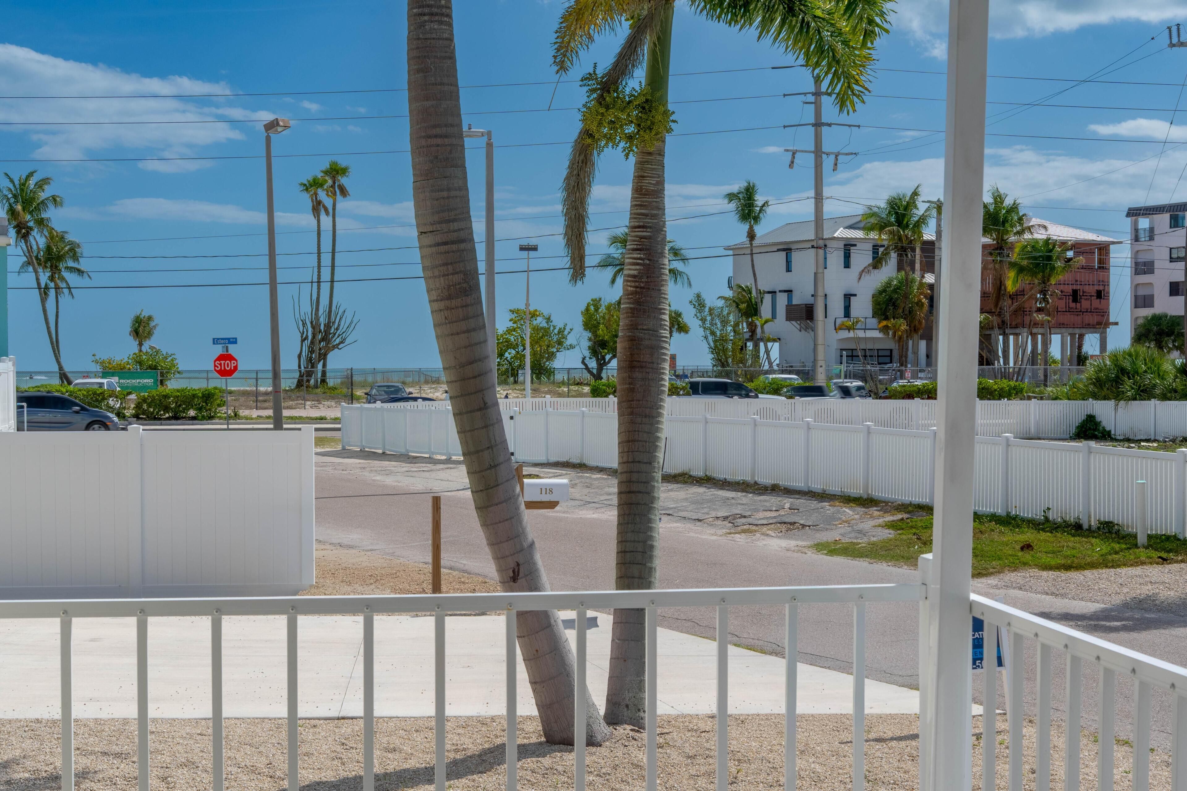A street view with palm trees, a stop sign, and a white fence.