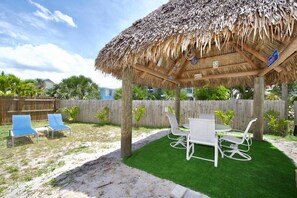 A covered outdoor seating area with a thatched roof, surrounded by a wooden fence, and featuring a table and chairs. - Lucky Charm (Fort Myers Beach)
