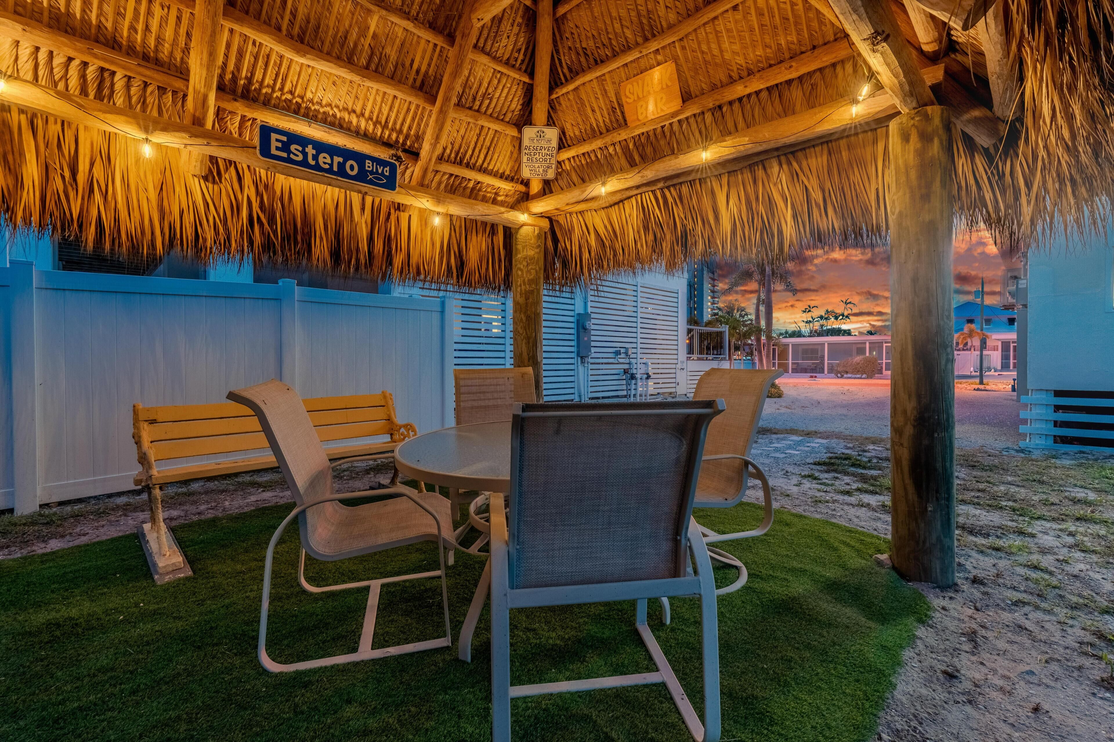 A covered outdoor seating area with a thatched roof, a sign for 'Estero Blvd', and a 'SNACK BAR' sign.