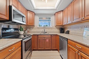 A kitchen with wooden cabinets, stainless steel appliances, a window, and a tiled backsplash. - Beach Bungalow (Fort Myers Beach)