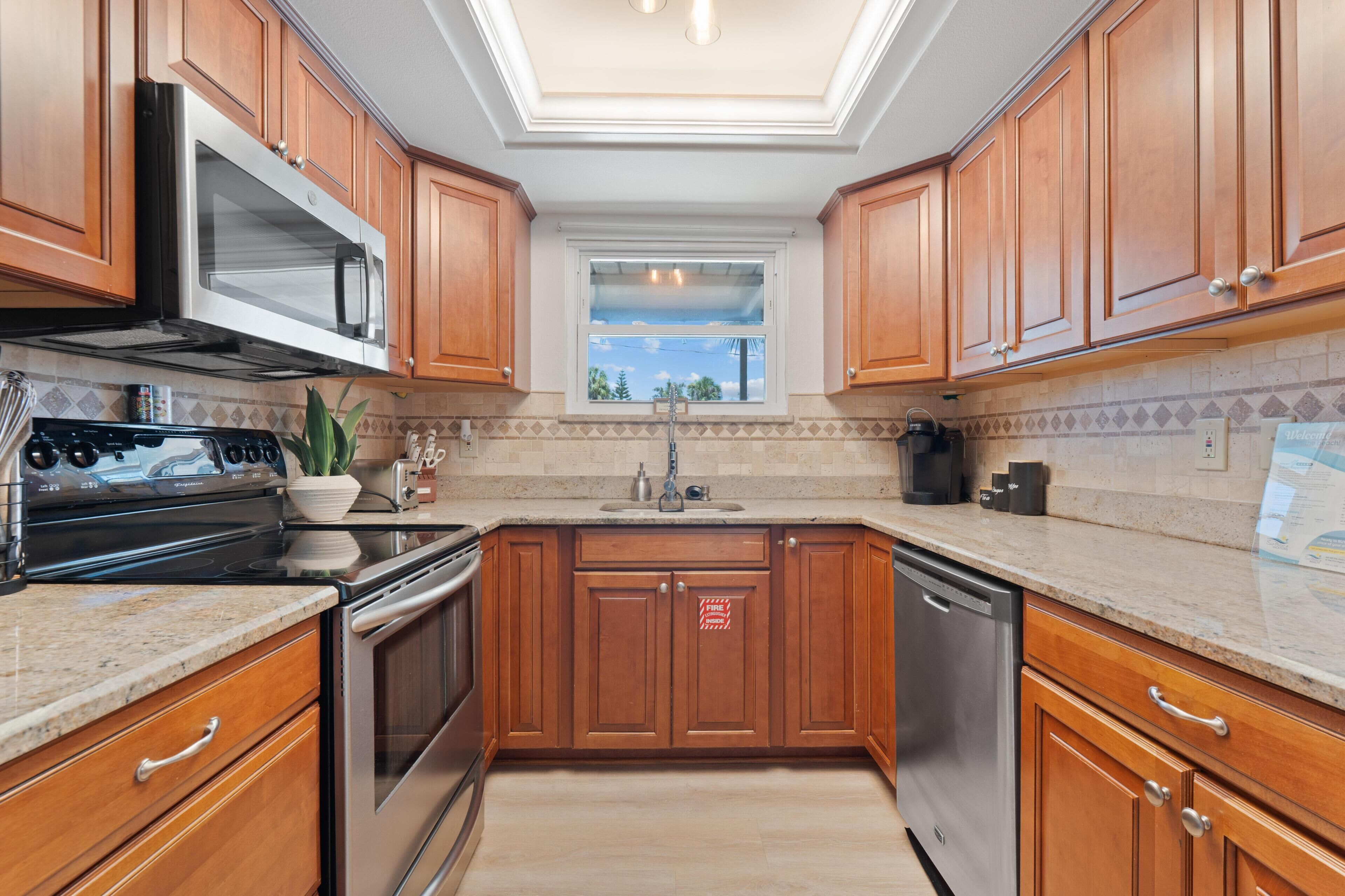 A kitchen with wooden cabinets, stainless steel appliances, a window, and a tiled backsplash.