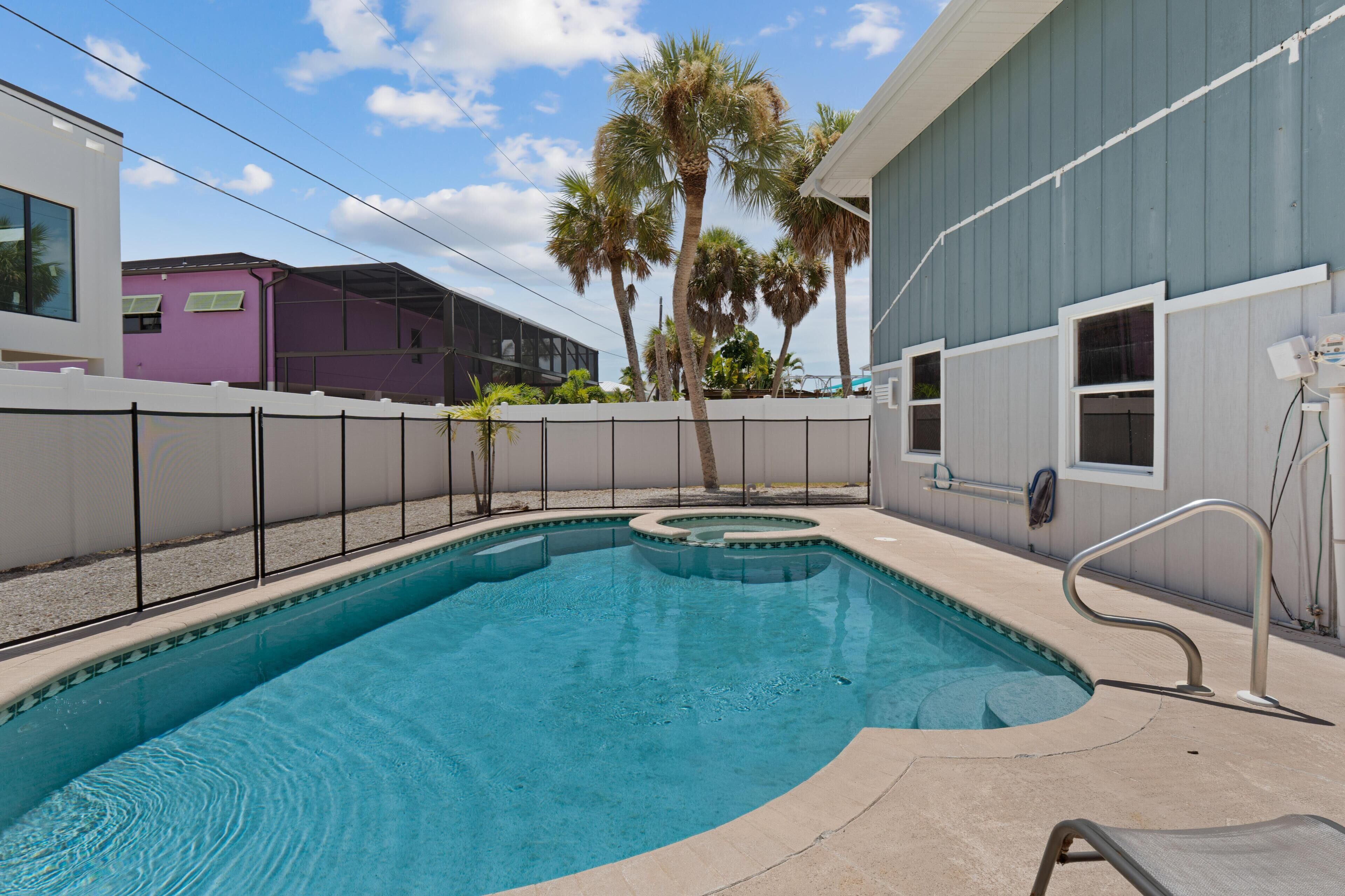 A swimming pool with a curved design, surrounded by a white fence and palm trees.