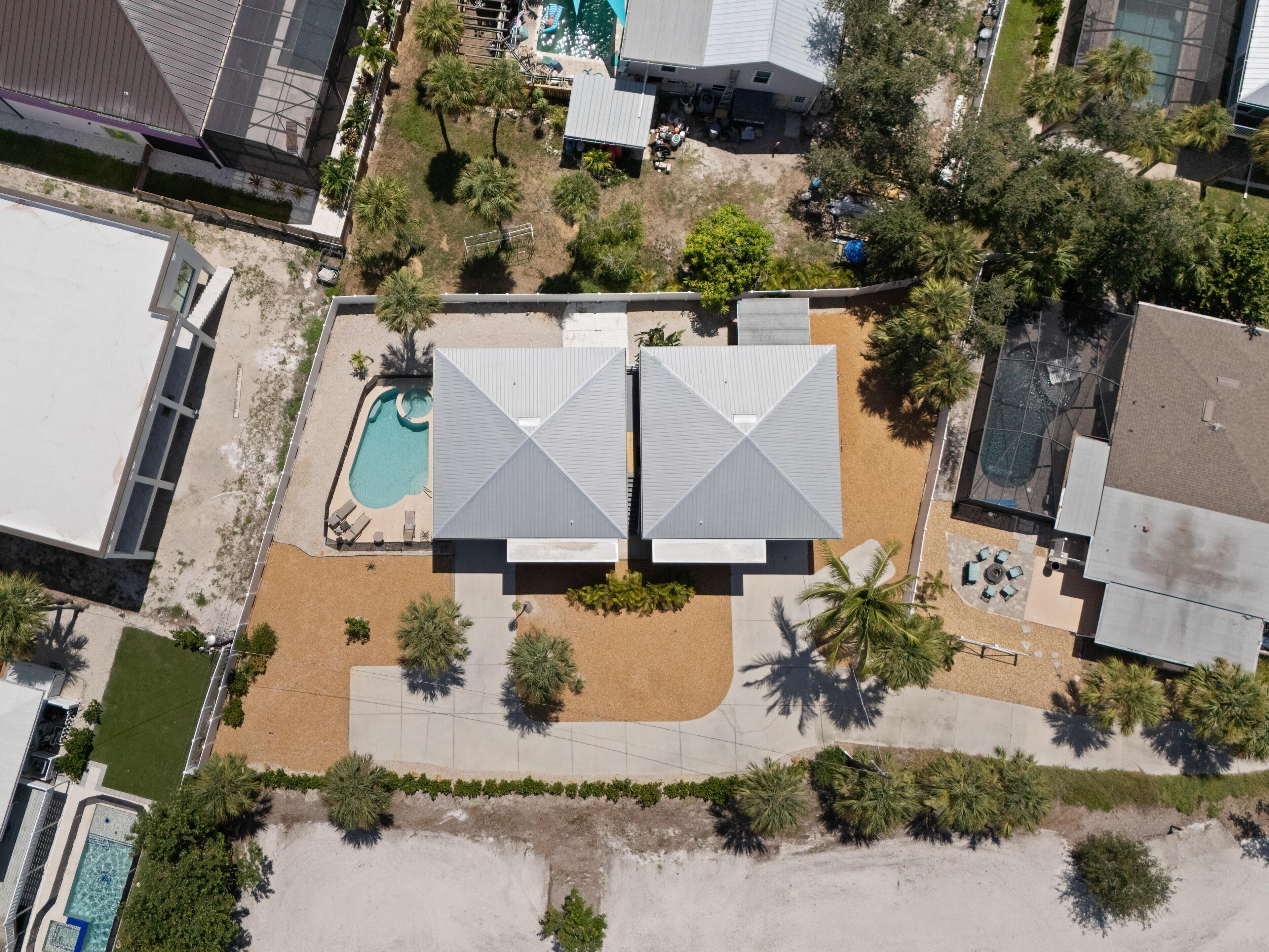 An aerial view of a property with a swimming pool, two large buildings with cross-shaped roofs, and surrounding greenery.