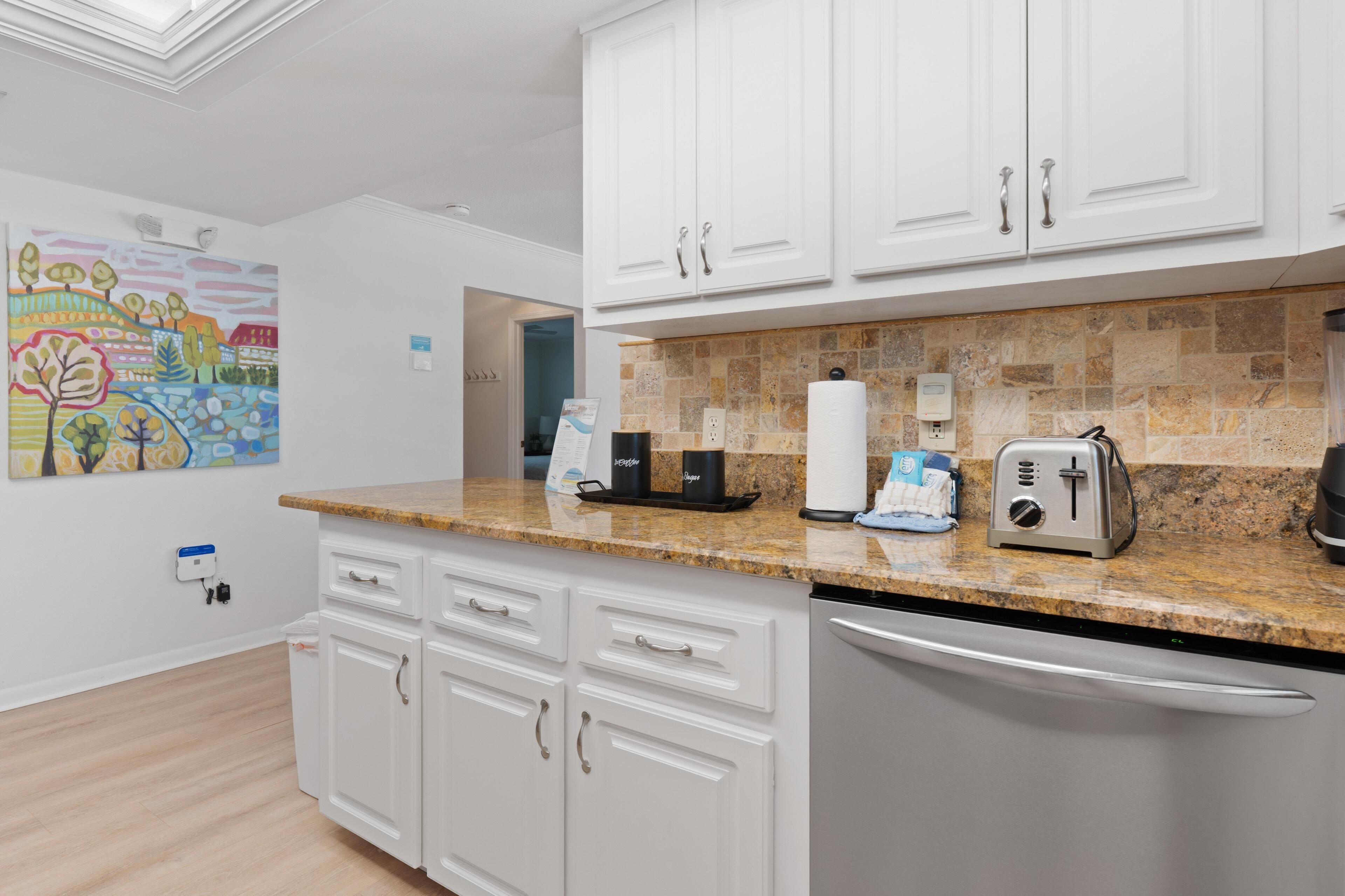 A modern kitchen with white cabinetry, a granite countertop, and a stainless steel dishwasher.