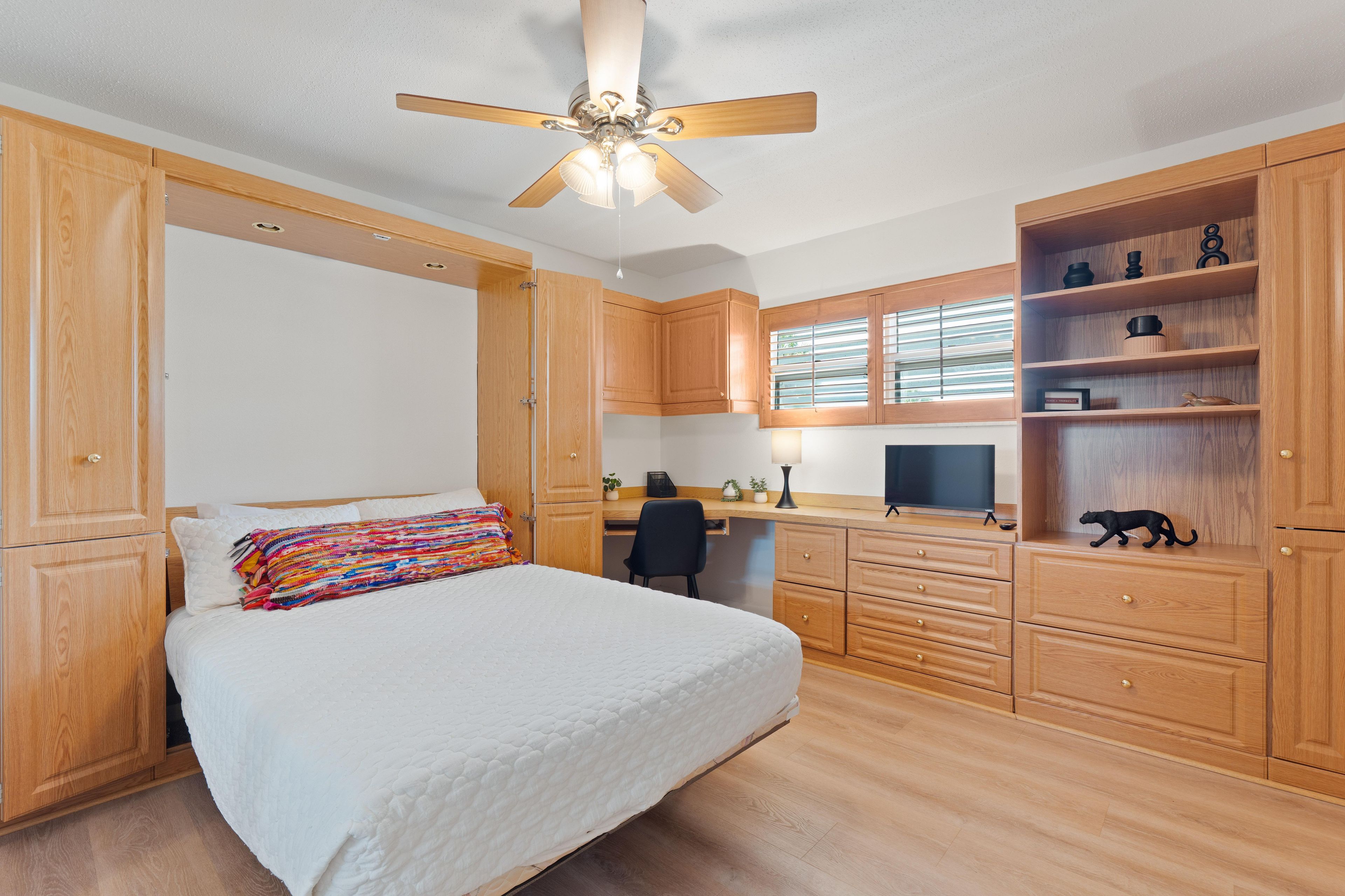 A bedroom with a bed, a desk, a chair, a TV, and wooden cabinets.