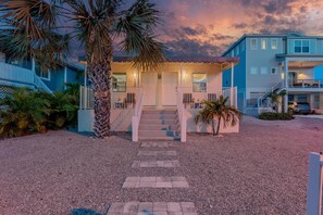 A coastal property with a covered porch, a staircase leading to the entrance, and a driveway.