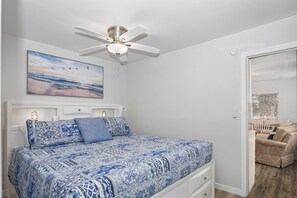 Een slaapkamer met een bed, een plafondventilator, een schilderij en een deur naar een andere kamer.