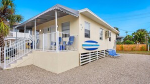 A single-story building with a covered porch, a small deck, and a blue surfboard mounted on the wall. - Lucky Charm 2 (Fort Myers Beach)