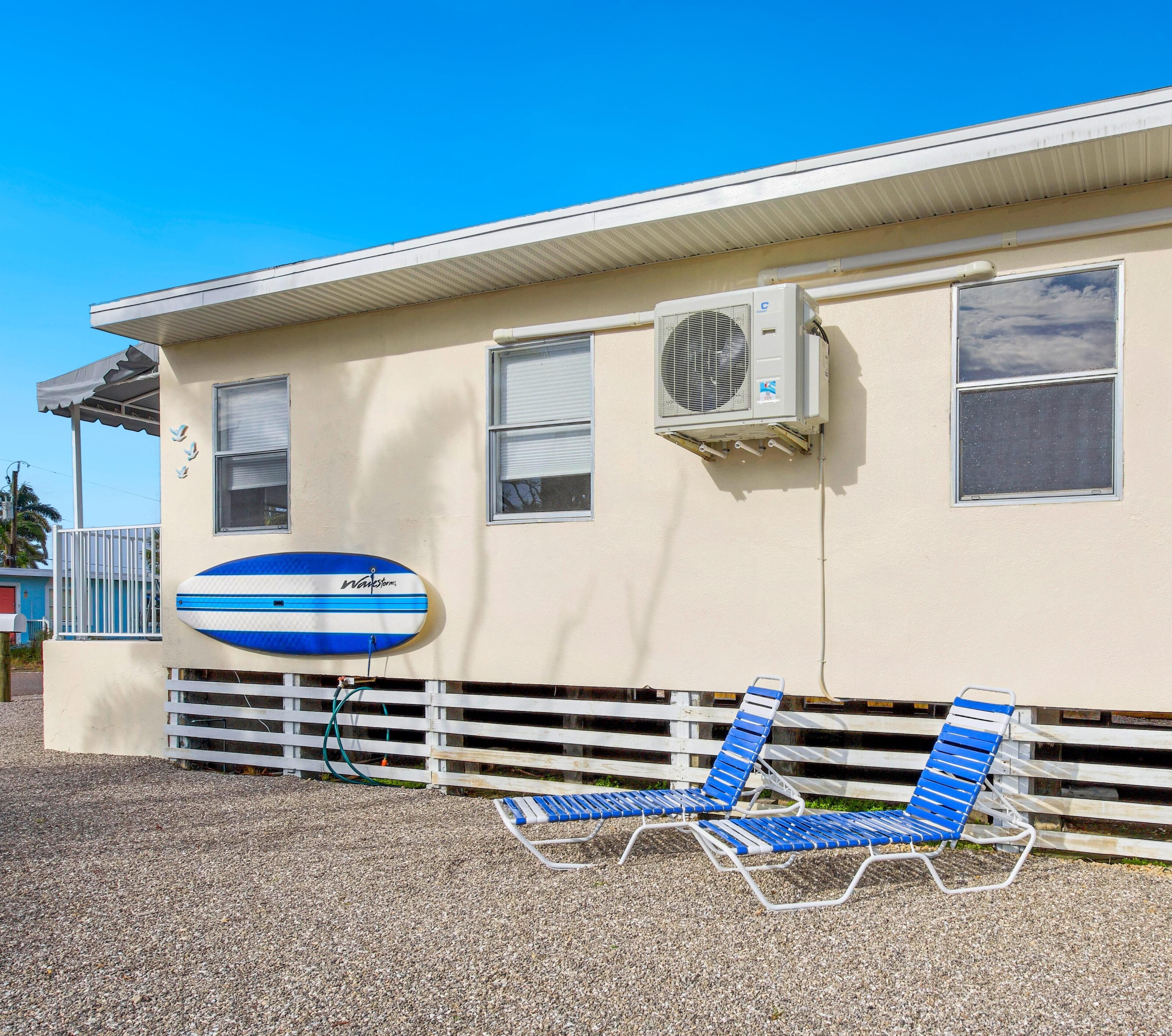 A beach house with a pool, two lounge chairs, and a large blue surfboard.