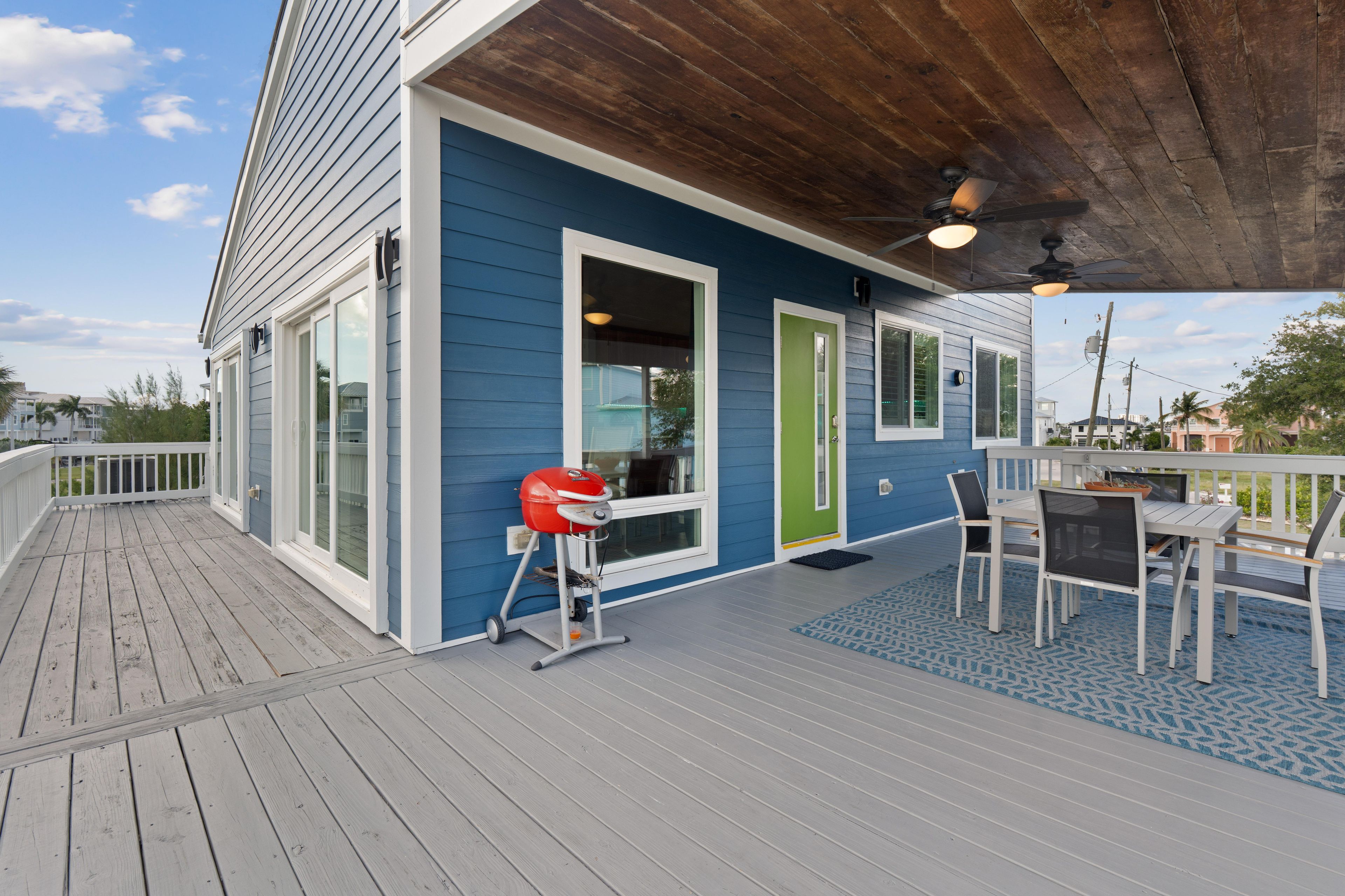 A covered deck with a barbecue grill, outdoor seating, and a view of the surrounding neighborhood.
