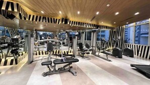 Un gimnasio moderno con varios equipos de ejercicio, techo de madera y ventanas amplias.