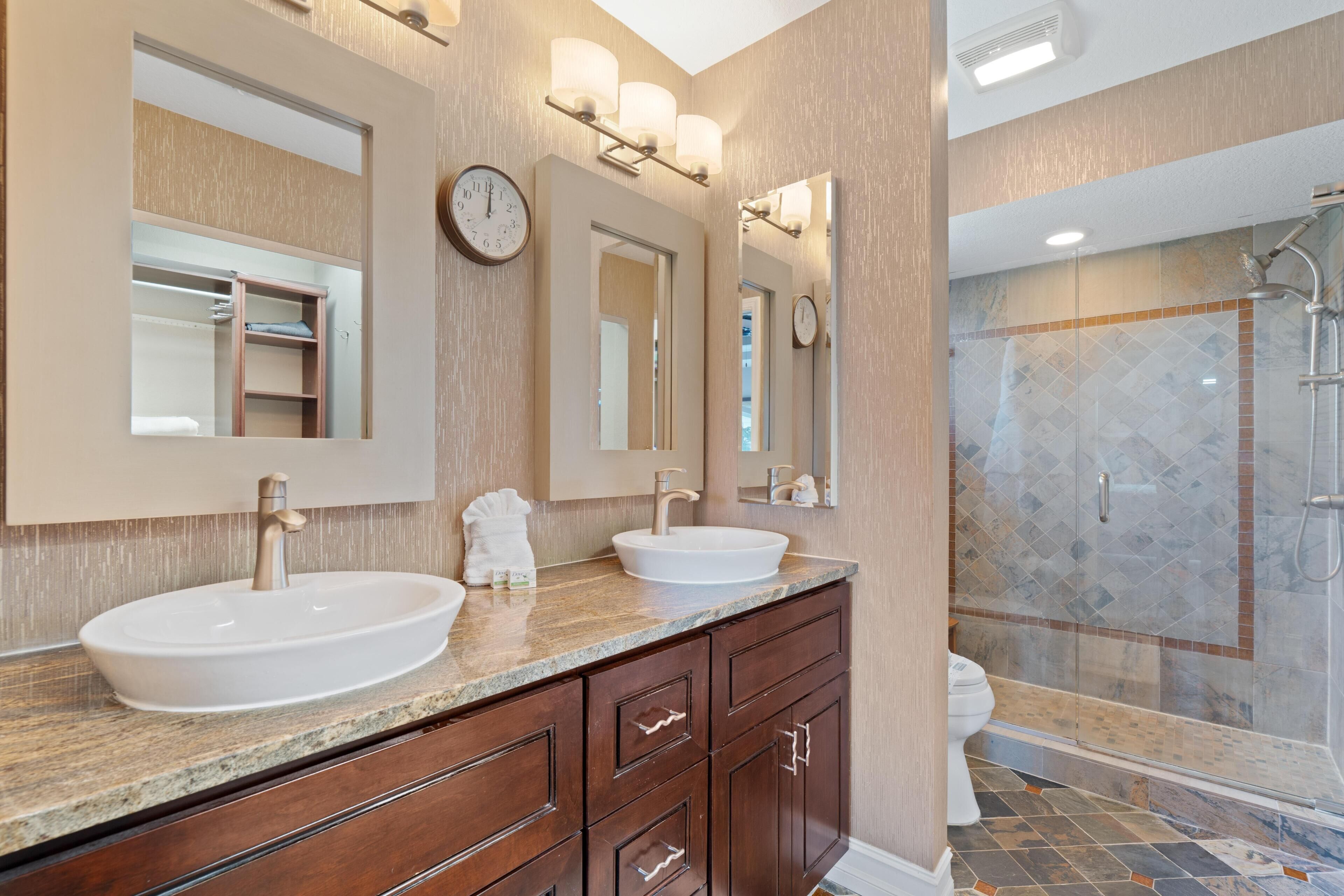 A bathroom with two sinks, a mirror, a clock, and a shower area.