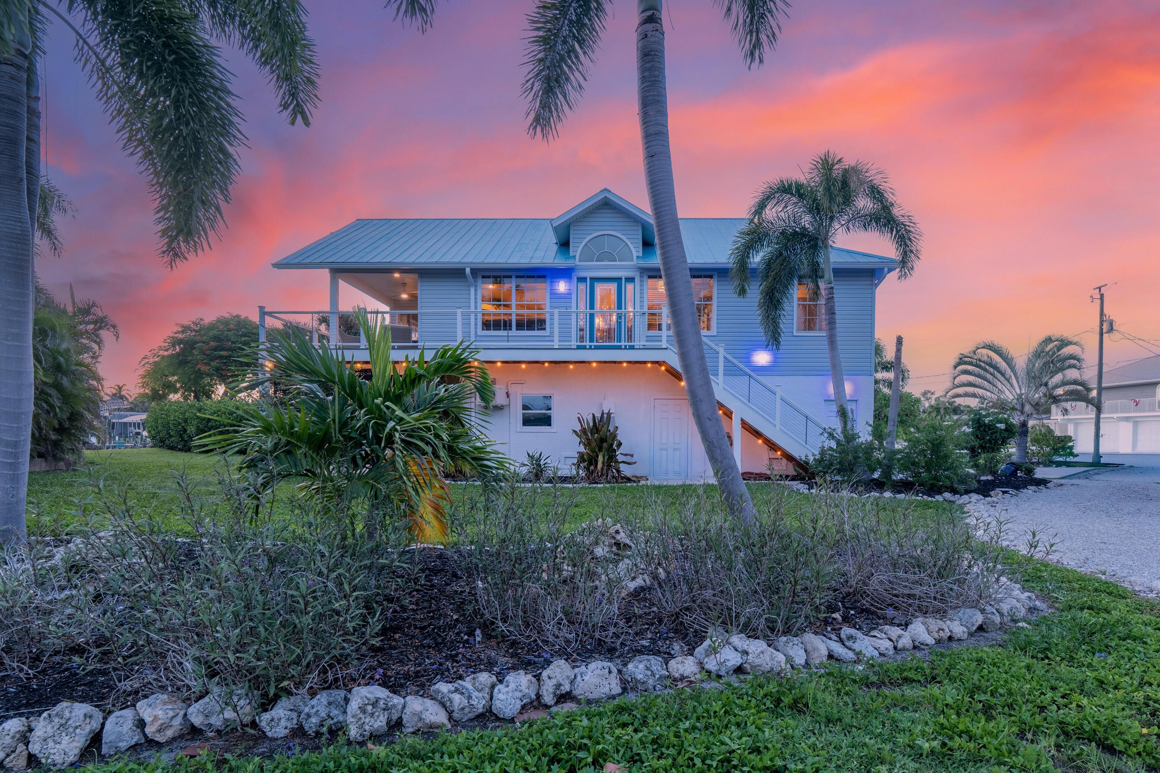 A two-story house with a balcony, surrounded by tropical vegetation.