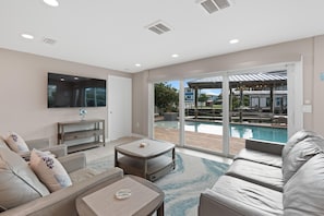 A modern living room with a pool view, a flat-screen TV, and a comfortable seating area. - Kokomo (Fort Myers Beach)