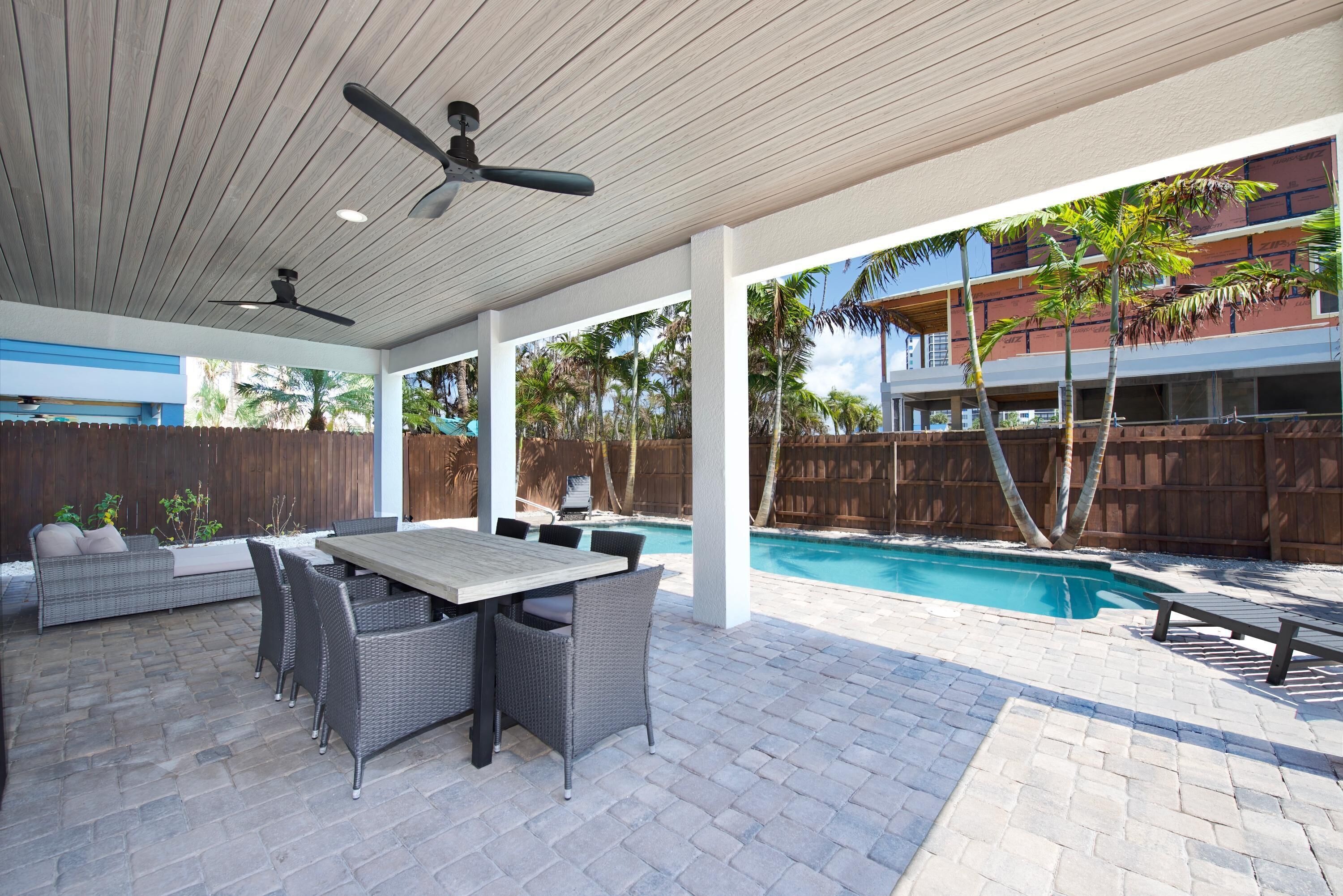 An outdoor patio with a pool, covered seating, and ceiling fans.