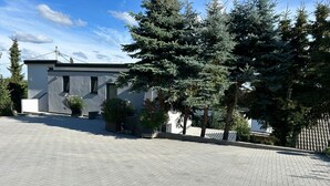 A modern building with a paved driveway, potted plants, and a row of evergreen trees. - Modern vacation home in the countryside and close to the city! (Koblenz)