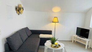 A modern living room with a grey sectional sofa, a white coffee table with decorative items, a floor lamp, and a TV on a white stand. - Modern vacation home in the countryside and close to the city! (Koblenz)