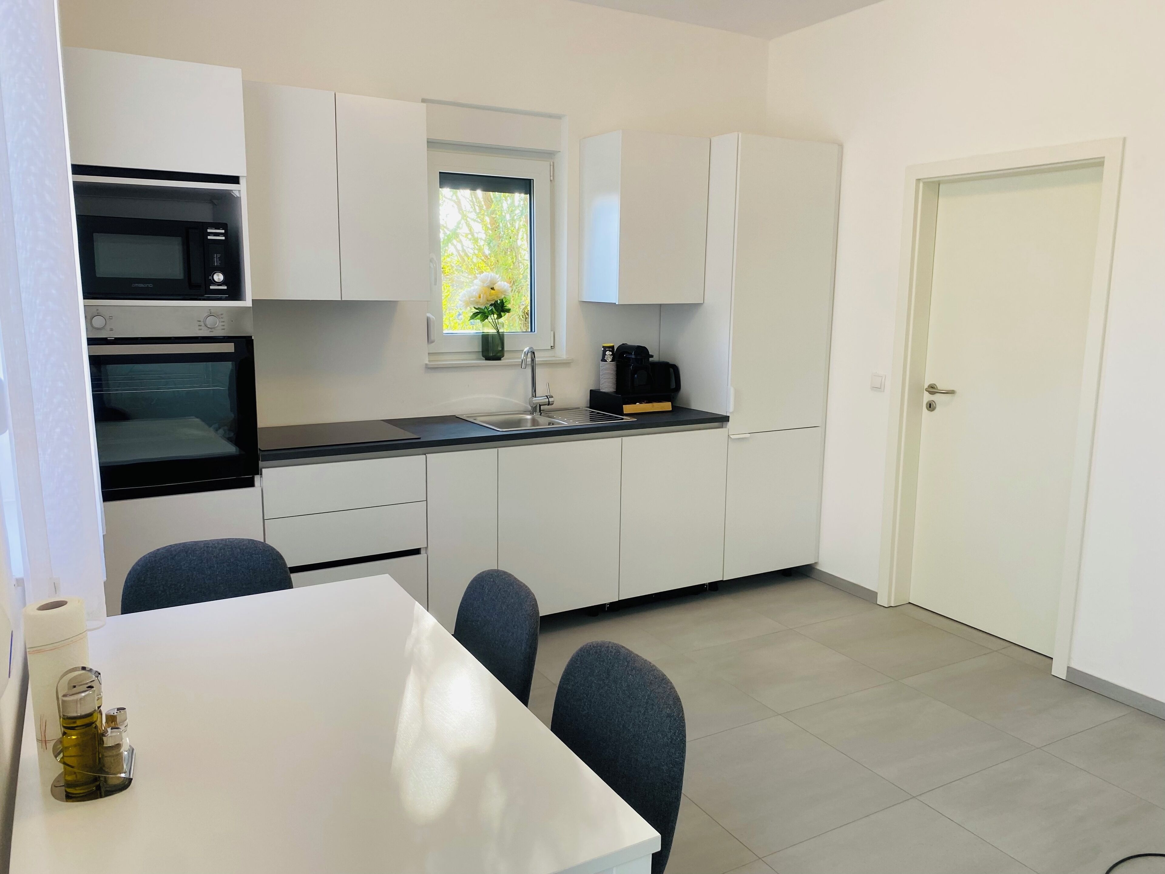 A compact kitchen with white cabinets, a built-in microwave, a coffee maker, and a window with a plant.