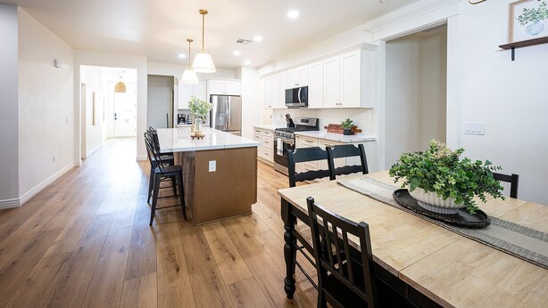 A modern kitchen with white cabinets, a central island, and a dining area with a wooden table and chairs.