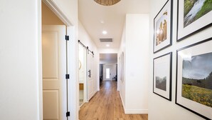 A hallway with wooden flooring, white walls, and framed pictures on the right.