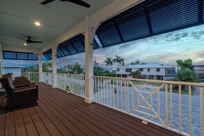 A covered outdoor area with a wooden deck, white railings, and a view of the surrounding neighborhood. - Crain's Perch (Fort Myers Beach)