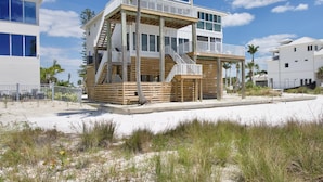 A multi-story beach house with a wooden deck, a balcony, and a staircase leading to the upper levels. - Lone Palm Retreat (Fort Myers Beach)