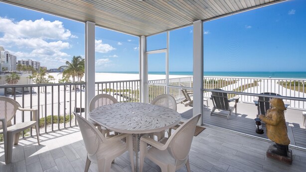 A covered outdoor area with a round table and chairs, a statue, and a view of the beach and ocean. - Lone Palm Retreat (Fort Myers Beach)