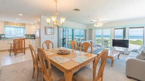 A spacious living room with a large dining table, comfortable seating, a TV, and a balcony with a view of the ocean. - Lone Palm Retreat (Fort Myers Beach)