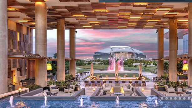 Een luxueuze hotellobby met een centrale fontein, terraszitplaatsen en uitzicht op een stadion.