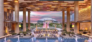 Een luxueuze hotellobby met een centrale fontein, terraszitplaatsen en uitzicht op een stadion.