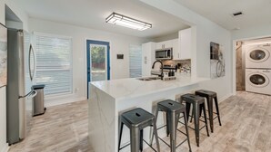 Een moderne keuken met een centraal eiland, barstoelen, een magnetron en een wasmachine.