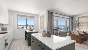 A modern kitchen with a large island, a dining area with a view, and a living space with a sofa and a plant. - The Kelly Residence @ Peninsula Village (Newport Beach)
