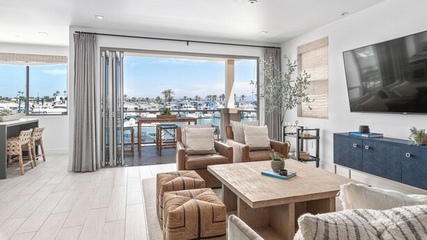 A spacious living room with a large TV, comfortable seating, a wooden coffee table, and a view of the marina. - The Kelly Residence @ Peninsula Village (Newport Beach)