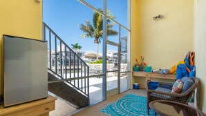 A room with a large window, a refrigerator, a wicker chair, and a small table. - Drift Inn (Fort Myers Beach)