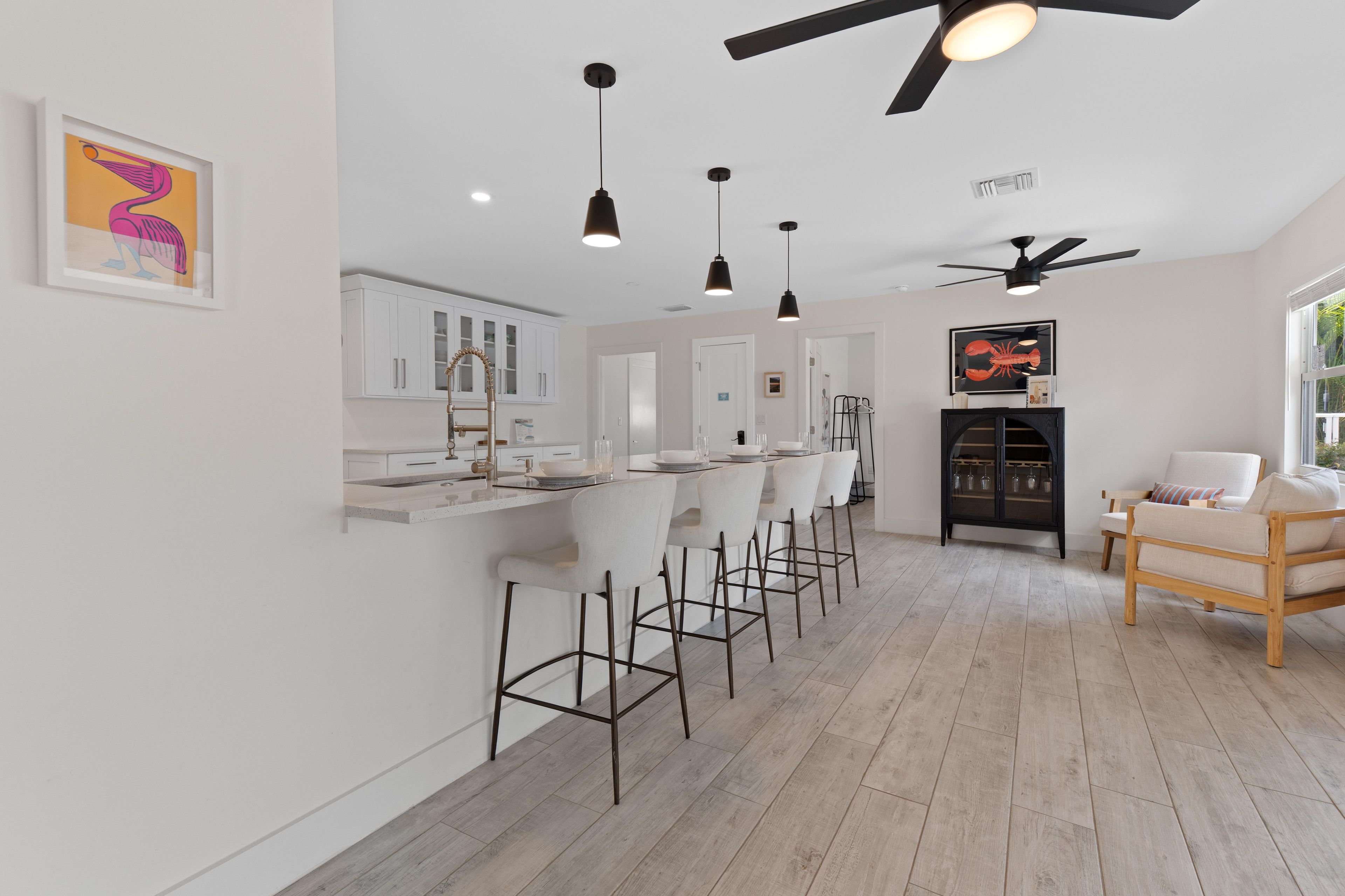 A modern kitchen with white cabinets, a bar area with stools, a ceiling fan, and a dining area with a wooden table and chairs.