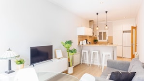 Una sala de estar moderna con televisor de pantalla plana, una mesa de comedor de vidrio y un sofá gris.