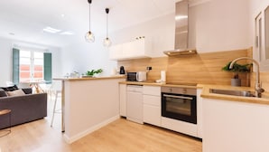 Una cocina moderna con armarios blancos, horno empotrado, pileta de acero inoxidable y lámparas colgantes.