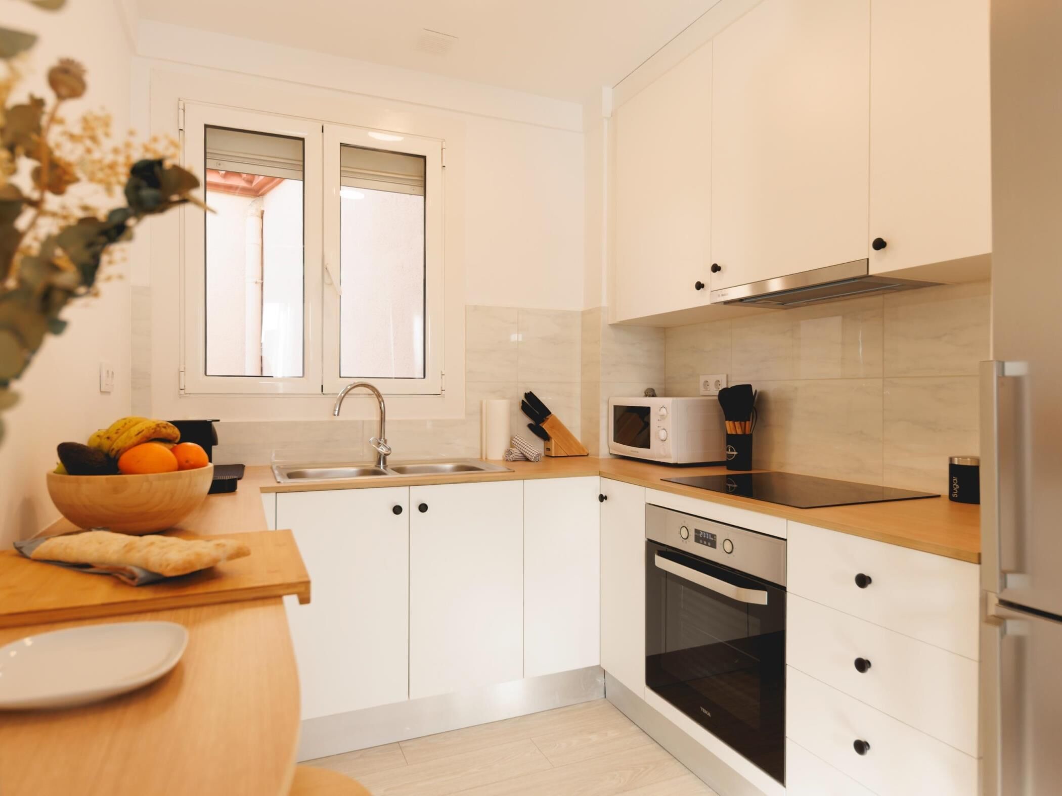 Une cuisine moderne avec des meubles blancs, un plan de travail en bois, un four encastré, un four à micro-ondes et un évier.