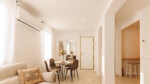 Een moderne woonkamer met een beige bank, een eettafel met stoelen en een keuken die door een open deur zichtbaar is.