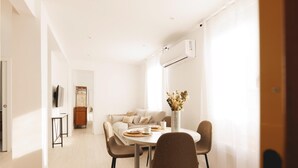 Een moderne woonkamer met een eethoek, voorzien van een zithoek, een eettafel met stoelen en een vaas met gedroogde bloemen.