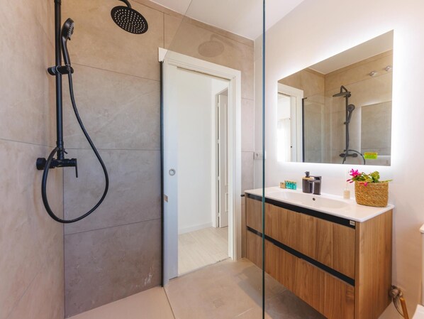 Un baño moderno con ducha, tocador con espejo y una puerta que da a otra habitación.