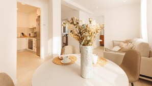 Een moderne woonkamer met een ronde eettafel, een vaas met gedroogde bloemen en een bank.