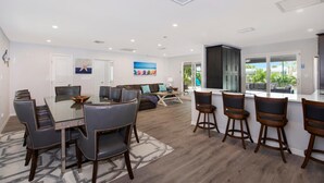 Une cuisine moderne dotée d’un grand îlot central, de chaises en bois foncé et d’un coin repas avec une table en verre et des chaises en cuir.