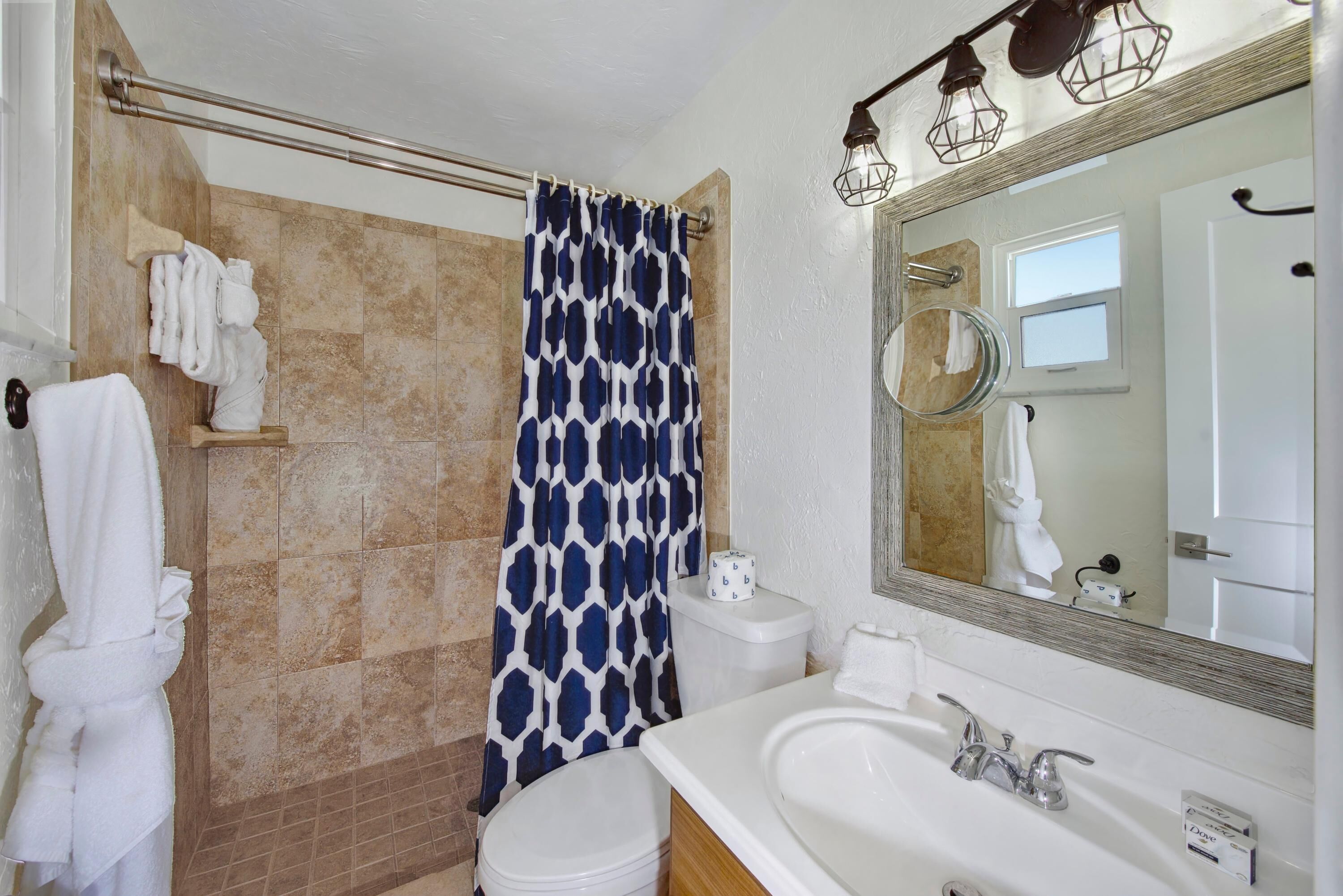 A bathroom with a shower curtain, a toilet, a sink with a mirror, and towels on a rack.