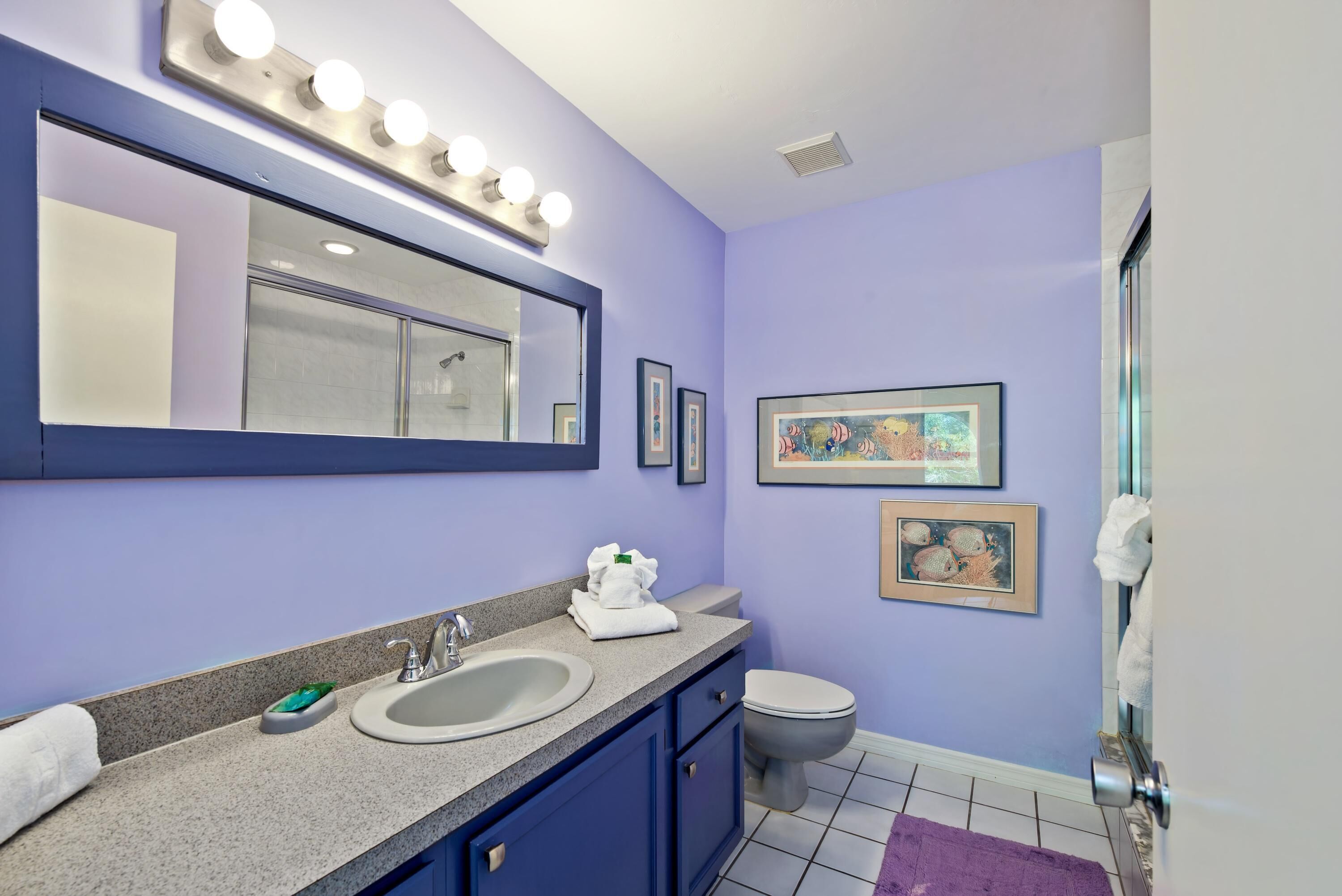 A bathroom with a vanity, sink, and toilet. There are lights above the mirror and framed pictures on the wall.