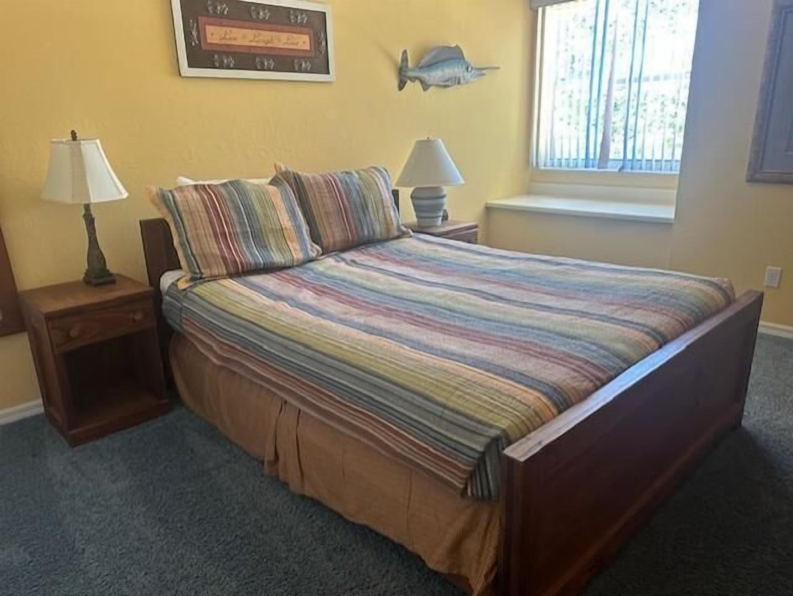Un dormitorio con cama, dos mesitas de noche, una ventana y adornos en la pared.