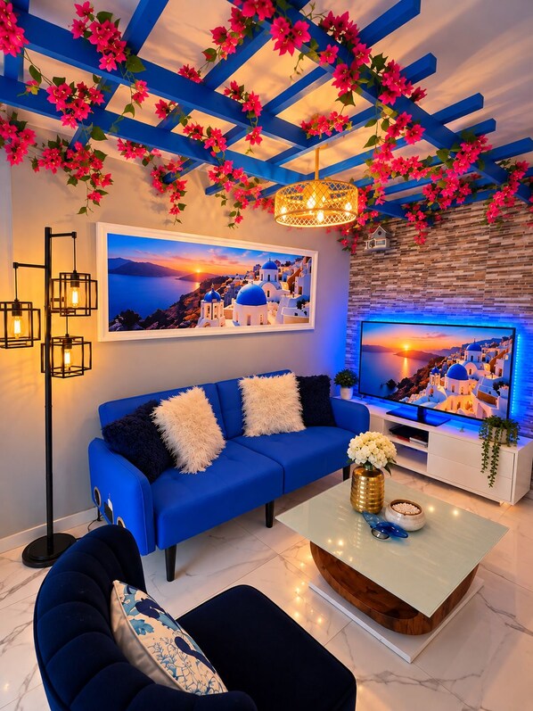 A modern living room with a blue sofa, a flat-screen TV, and a decorative ceiling with flowers.