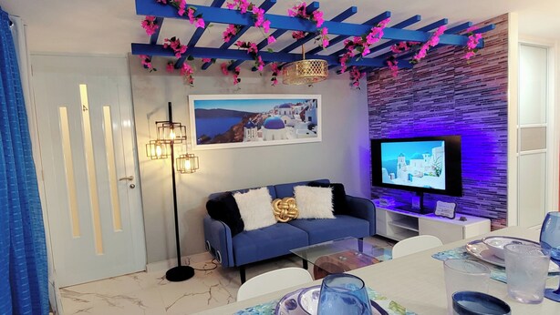 A modern living room with a blue sofa, a flat-screen TV, and a decorative ceiling with pink flowers. - Villa Santorini 3-bedroom apartment in welcoming Bayamón with WiFi, AC. Enjoy  (Bayamón)