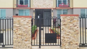 A multi-story residential building with a gated entrance, balconies with potted plants, and a stone facade. - Villa Santorini 3-bedroom apartment in welcoming Bayamón with WiFi, AC. Enjoy  (Bayamón)
