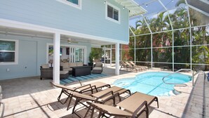 A poolside area with lounge chairs, a table, and a covered seating area with a sofa and chairs. - Gone Coastal (Fort Myers Beach)